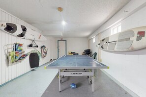 Taula de ping-pong en una habitació amb parets blanques, una sortida i diferent material esportiu.