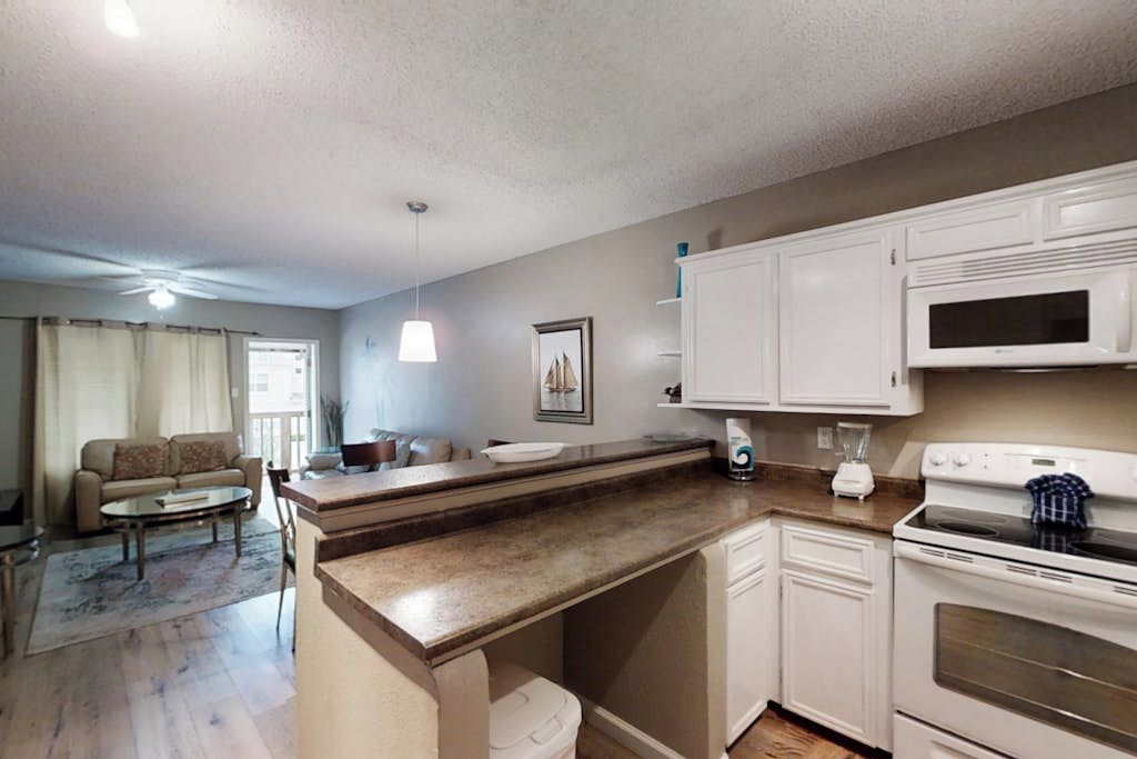 A compact kitchen with white cabinets, a microwave, and a stove. There is a dining area with a table and chairs, and a sofa.