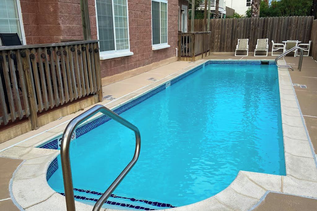 Una piscina rectangular con una escalera de metal, rodeada por un muelle de madera y un muro de ladrillo.