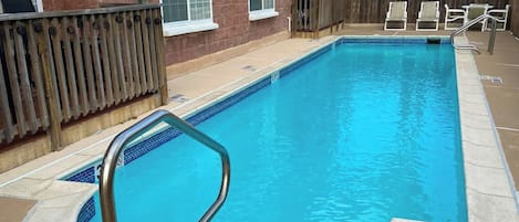 Una piscina rectangular con una escalera de metal, rodeada por un muelle de madera y un muro de ladrillo.