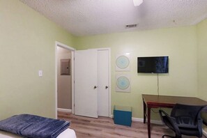 Ein Zimmer mit einem Bett, einem Schreibtisch, einem Stuhl, einem Fernseher und einer Tür.