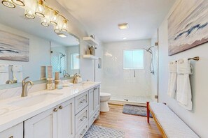 Een moderne badkamer met een grote spiegel, twee wastafels, een douche en een bankje.