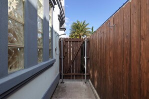 A narrow alleyway with a wooden gate, a concrete path, and a building with large windows on one side. - Retama Landing #3 - Pool & Balcony, Walk to Beach (South Padre Island)