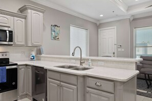 A kitchen with white cabinetry, a stainless steel sink, a microwave, and a dishwasher. - Retama Landing #3 - Pool & Balcony, Walk to Beach (South Padre Island)