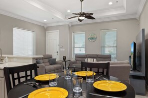 A dining area with a black table set for four, yellow plates, and clear glasses. - Retama Landing #3 - Pool & Balcony, Walk to Beach (South Padre Island)