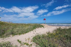 A beach with a flag on a pole, sandy dunes, and a clear sky. - Retama Landing #3 - Pool & Balcony, Walk to Beach (South Padre Island)