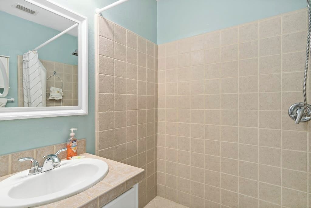 A bathroom with a sink, mirror, and shower.