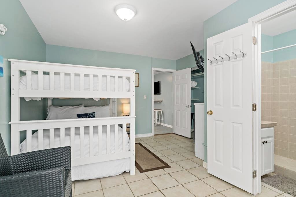 A room with a bunk bed, a door leading to a bathroom, and a small seating area.