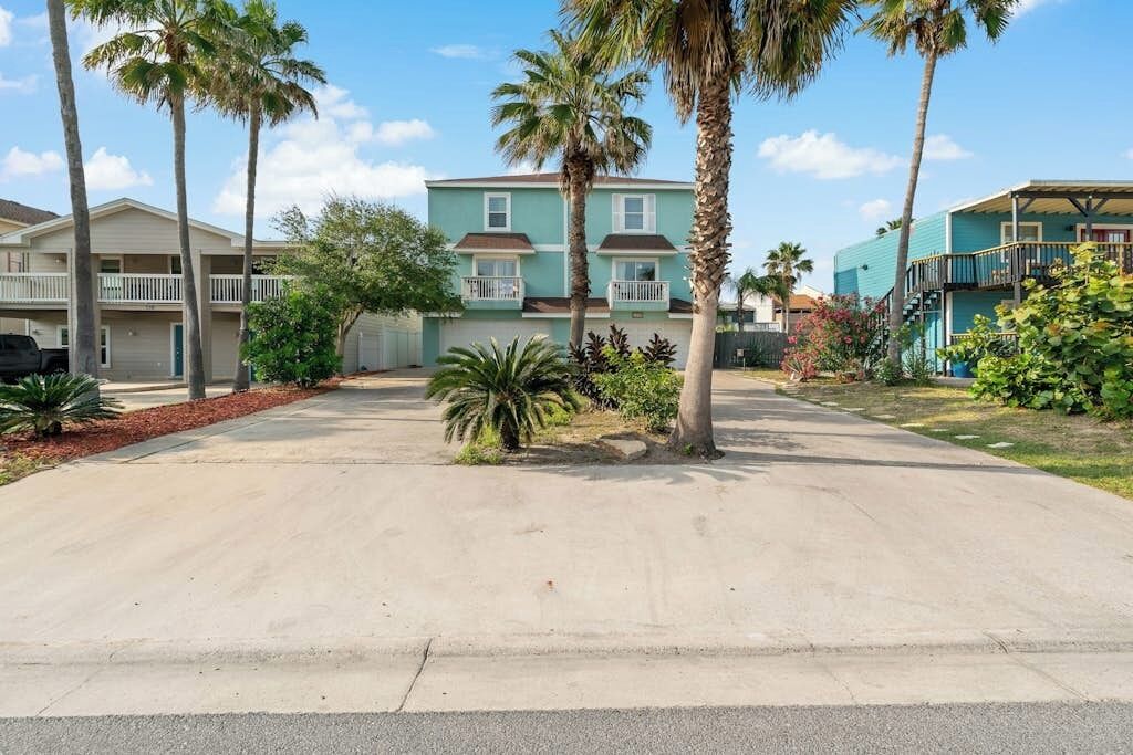 A residential area with two-story buildings, a paved driveway, and palm trees.