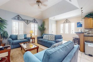 A living room with two sofas, a coffee table, and a kitchen area with wooden cabinets. - Garden Breeze Condominiums #3 (South Padre Island)