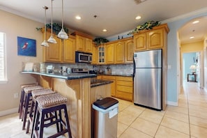 A kitchen with wooden cabinets, stainless steel appliances, and a bar area with stools. - Garden Breeze Condominiums #3 (South Padre Island)