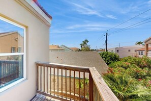 Un balcone abitativo con ringhiera in legno, affacciato su un giardino ricco di piante e un cielo sereno.