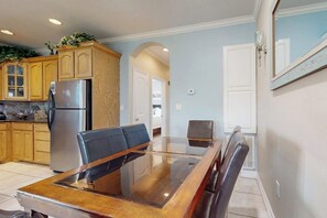 Un'area pranzo con un tavolo e sedie in vetro, mobili contenitori in legno e un frigorifero.