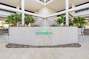 Een receptiezone met een palmboom logo en de naam 'SUNCHASE IV' op een witte achtergrond.