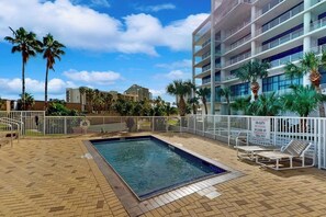 A swimming pool area with a fenced deck, lounge chairs, and palm trees. - Sunchase IV #316 - Heated Pool & Ocean Views (South Padre Island)
