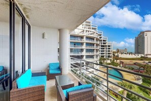 A balcony with wicker furniture, a pool, and a view of a multi-story building. - Sunchase IV #316 - Heated Pool & Ocean Views (South Padre Island)