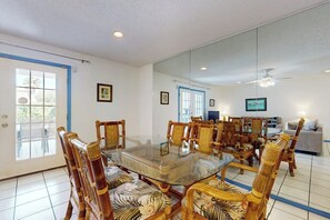 A dining area with a glass-top table surrounded by wooden chairs with floral upholstery. - Mars Island Unit B - Private Pool, Walk to Beach (South Padre Island)