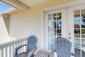 A covered porch with two Adirondack chairs and a white door with glass panels. - Mars Island Unit B - Private Pool, Walk to Beach (South Padre Island)