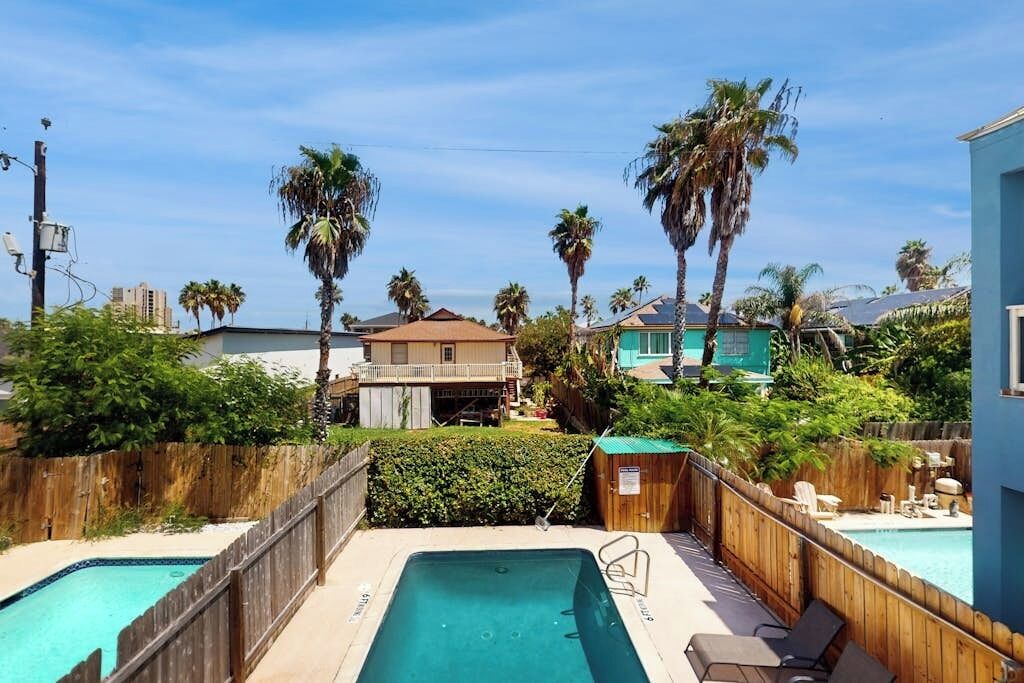 Un patio trasero con piscina, cerca de madera y palmeras.