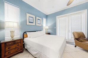 A bedroom with a bed, nightstands, a chair, and a door. - Saturn Serenity 1 - Shared Pool & Dog-Friendly (South Padre Island)
