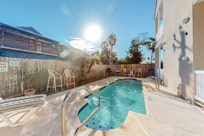 A swimming pool with a wooden fence, lounge chairs, and a building in the background. - Saturn Serenity 1 - Shared Pool & Dog-Friendly (South Padre Island)