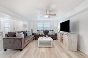 A modern living room with a grey sofa, a white coffee table, and a flat-screen TV on a wooden cabinet. - Lazy Seagull Beach House - Downstairs (South Padre Island)