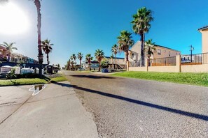 Rua residencial com casas, palmeiras e céu ensolarado.