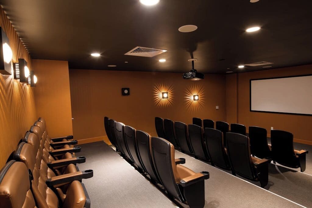 A conference room with rows of chairs, a projector screen, and wall-mounted lighting.