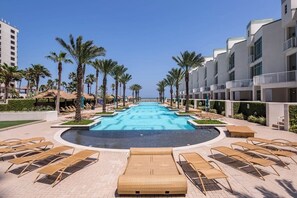 Zona de piscina con sillas de descanso y palmeras, rodeada de edificios de hotel.