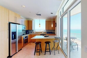 A modern kitchen with a large island, stainless steel appliances, and a view of the ocean. - Sapphire Condominiums #2701 (South Padre Island)