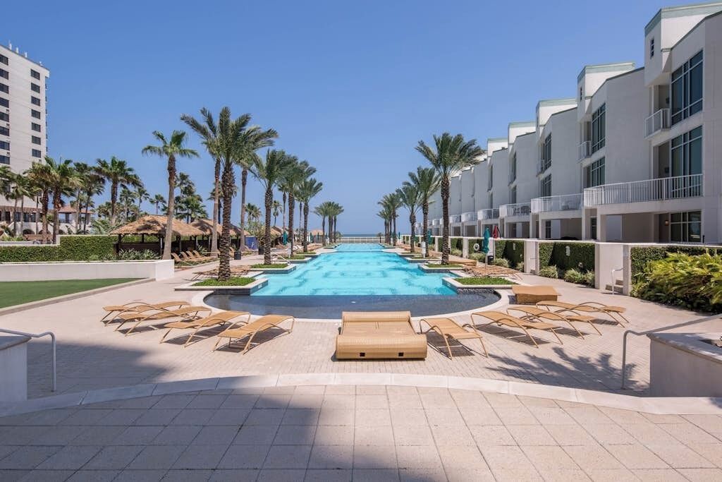 A swimming pool with lounge chairs and palm trees, surrounded by modern buildings.