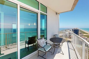 A balcony with a table and chairs, overlooking a cityscape and the ocean. - Sapphire Condominiums #2701 (South Padre Island)