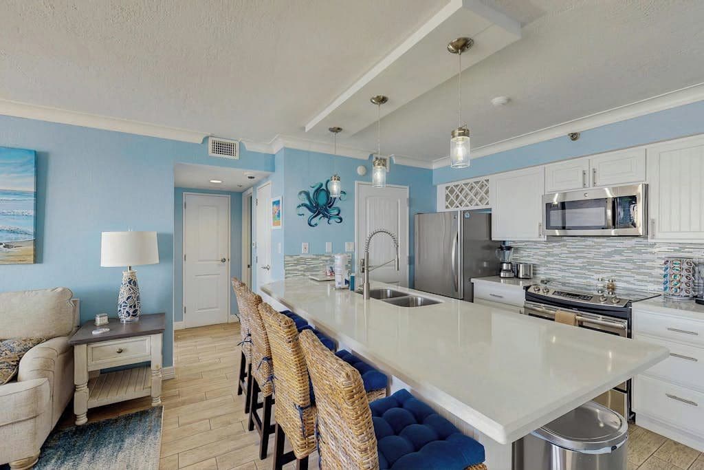 Una cocina moderna con una isla central, muebles blancos, electrodomésticos de acero inoxidable y una pared de acento azul.