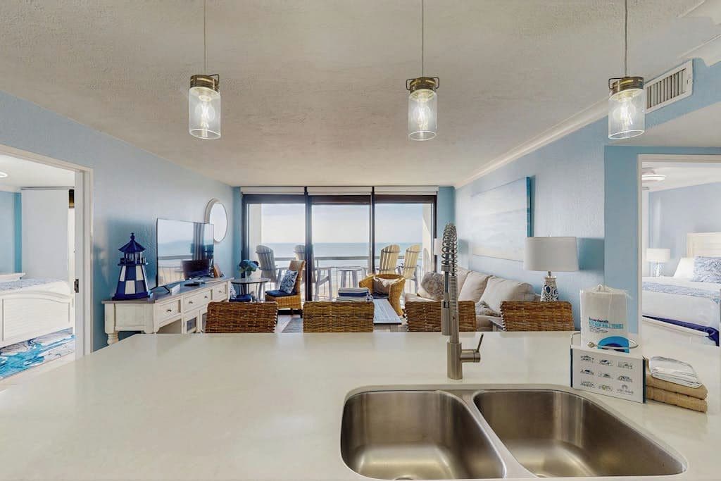 A modern hotel room with a large window, a kitchenette, a dining area, and a bathroom.