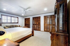 A bedroom with a bed, a ceiling fan, wooden shutters, and a large window. - Anchors Away at North Shore (Port Isabel)