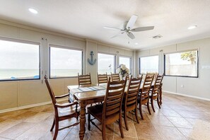 A dining area with a table and chairs, large windows with ocean views, a ceiling fan, and a brick wall. - Anchors Away at North Shore (Port Isabel)