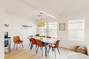 A modern kitchen with a dining area, featuring a large table, chairs, and a hanging light fixture. - Lounging by the Sea - Ocean Views, Steps to Beach (Galveston)