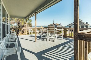 A covered outdoor area with a wooden deck, white plastic chairs, and a view of the beach. - Lounging by the Sea - Ocean Views, Steps to Beach (Galveston)