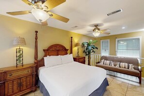 A hotel room with a large bed, two bedside tables, a wooden headboard, a ceiling fan, a bench, and a potted plant. - Sailor's Dream - Waterfront, Boat Slip & Dogs OK (Port Isabel)