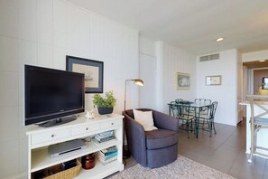 A living room with a flat-screen TV, a white entertainment unit, a grey sofa, a dining table with chairs, and a lamp. - La Playa Condominiums 209 (South Padre Island)