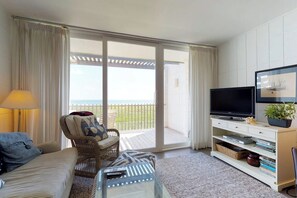 A living room with a sofa, armchair, TV, and a balcony with a view. - La Playa Condominiums 209 (South Padre Island)