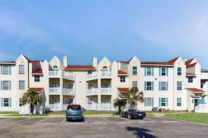 A multi-story hotel with a central courtyard, balconies, and a parking lot. - Beach Club - The Lighthouse (Corpus Christi)