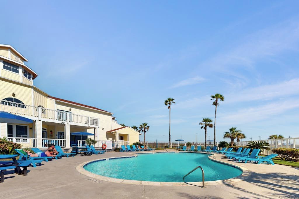 A pool area with lounge chairs and a building with balconies.