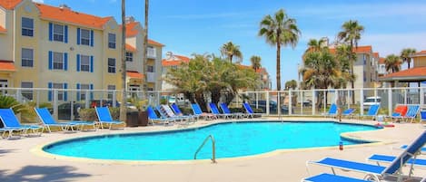 Una piscina con sillas reclinables y palmeras, rodeada de edificios de varios pisos con balcones.