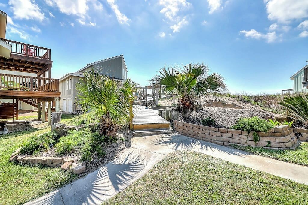 A residential property with a paved driveway, a wooden deck, and a landscaped garden with palm trees.