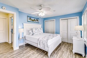 Ein Schlafzimmer mit einem Bett, einem Deckenventilator, einem Nachttisch und einer Wandleuchte.
