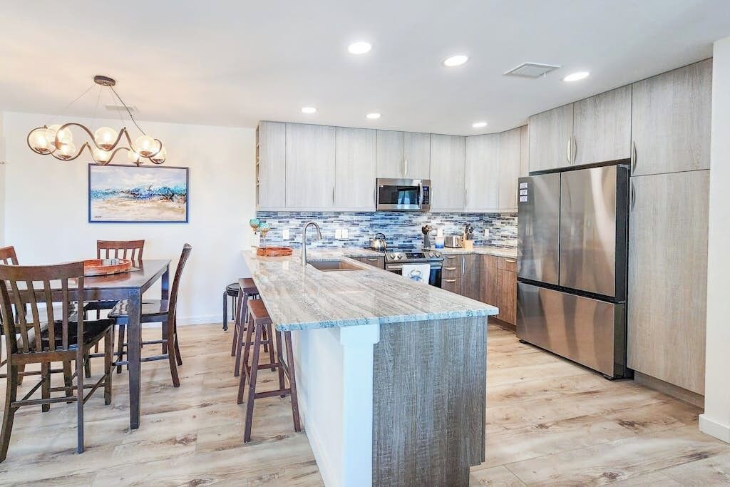 A modern kitchen with a central island, stainless steel appliances, and a dining area with wooden chairs.