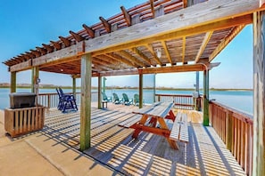 Eine Holzterrasse mit Picknicktischen und -stühlen, die auf ein Gewässer blickt.