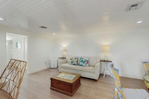 A living room with a white sofa, two lamps, a wooden coffee table, and a wicker chair. - El Cerrito Place - Rooftop Deck & Historic Charm (Port Aransas)