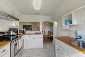 Cozinha moderna com armários brancos, micro-ondas, fogão e pia. É possível ver uma área de jantar com cadeiras e uma mesa ao fundo.